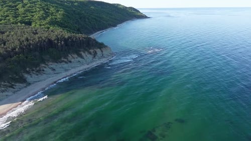 Beach Between a Ledge Covered with Vegetation and a Black Sea Under a Clear Blue Sky