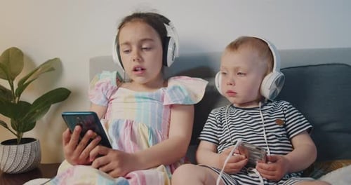 Siblings Using Phones and Wearing Headphones Indoors