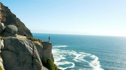 Drone, man on cliff and mountain, ocean and environment with blue sky, waves and hiking path