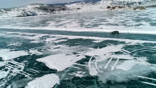 Aerial Side View on a Car Driving on an Ice Road on Frozen Baikal Winter Landscape of Lake Baikal