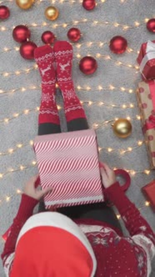 Woman Wrapping Christmas Gift on Floor with Lights