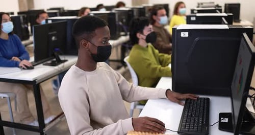 Young Multiracial Students Using Computers Inside College Class Room While Wearing Safety