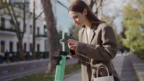 Young Businesswoman Checking Phone By Electric Scooter in City