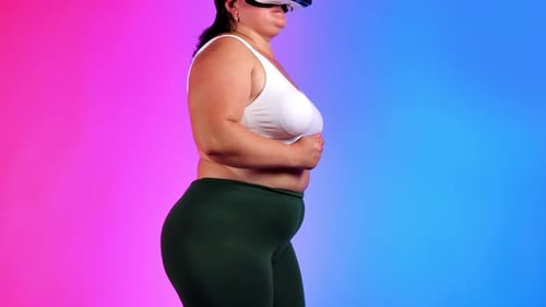 Woman with overweight in a tracksuit and VR headset doing exercises in a studio with blue and red ba