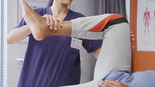 Diverse female physiotherapist and senior male patient in hospital physical therapy session on leg