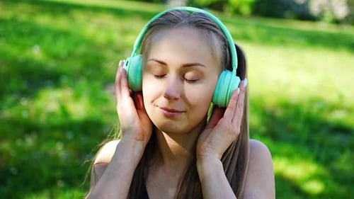 Young Woman Wearing Wireless Headphones Listens to Music in City Summer Park