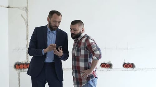 Agent with Client Talking About Project and Using Smartphone at New Home Adult