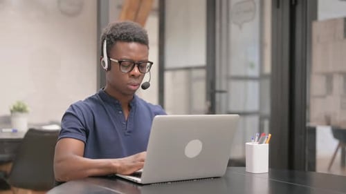 Young African Man with Headset Working on Laptop in Call Center