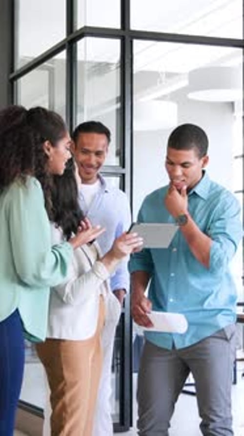 Vertical video: Diverse coworkers tapping tablet, highfiving after Hispanic woman entering office