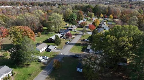 Aerial flyover quaint suburb neighborhood with colored trees in fall season. Beautiful sunny day in
