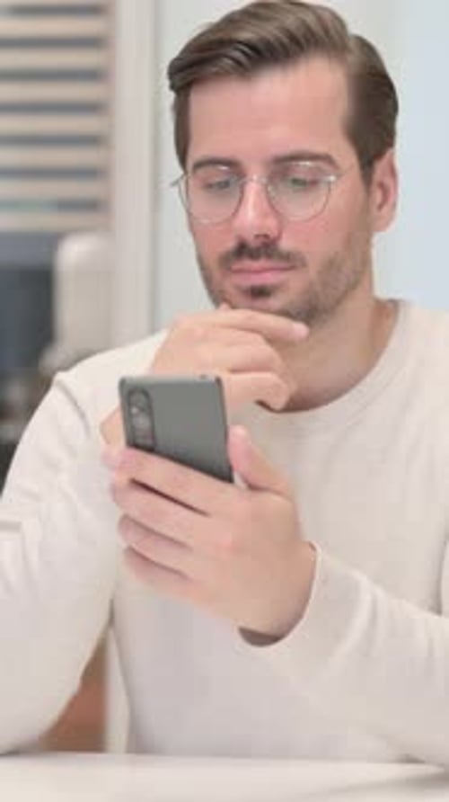 Junger Mann surft im Büro am Telefon im Internet