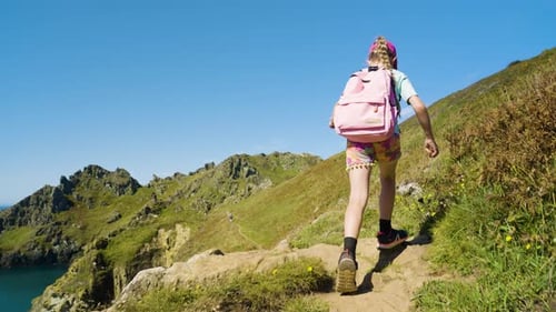 Young Girl In Colourful Clothes Walking On Hiking Path Along Beautiful Coastal Hills