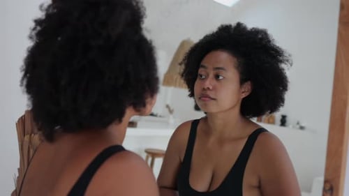 Lockige Afroamerikanerin betrachtet sich im Spiegel Die Frau mag ihr Gesicht und ihren Körper
