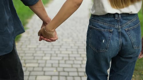 A Young Positive Couple Walks Holding Hands Meets in a Summer City Park