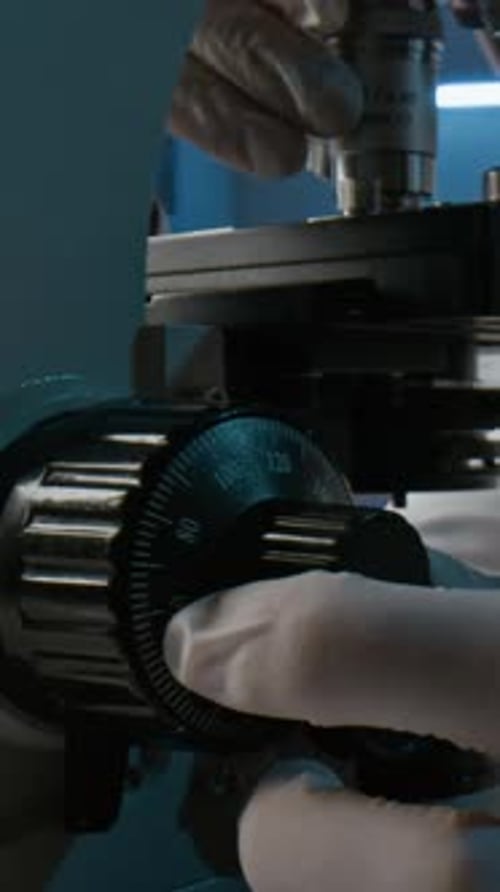 Hands Adjusting Microscope in Dark Lab Close Up