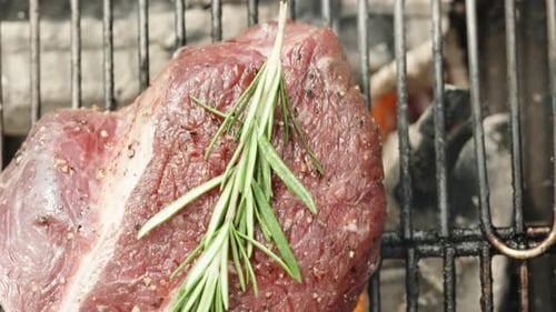 The beef steak, accompanied by a sprig of rosemary, sizzles on the charcoal grill