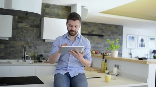 Young man works on tablet at kitchen countertop in sunny home office