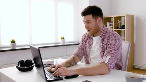 Excited man using laptop at desk in bright room