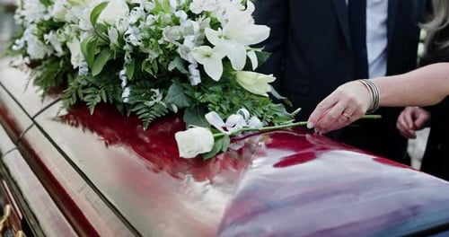 Hand, coffin and flowers for funeral at cemetery, memorial service and pay respect with family