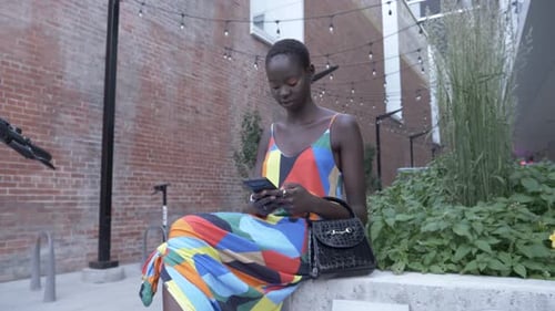 Stylish young woman in dress uses smart phone in urban city courtyard