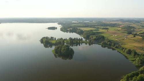 View of a scenic lake with sun reflection and surrounded by green farmland.