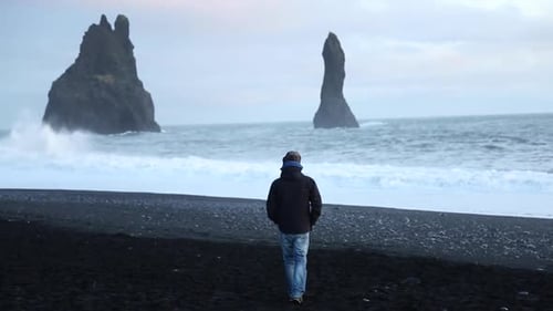 Man walking on a dark beach. Dýrahólaey, beach in southern Iceland