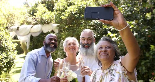 Taking selfie, senior friends celebrating with champagne at outdoor wedding, smiling happily