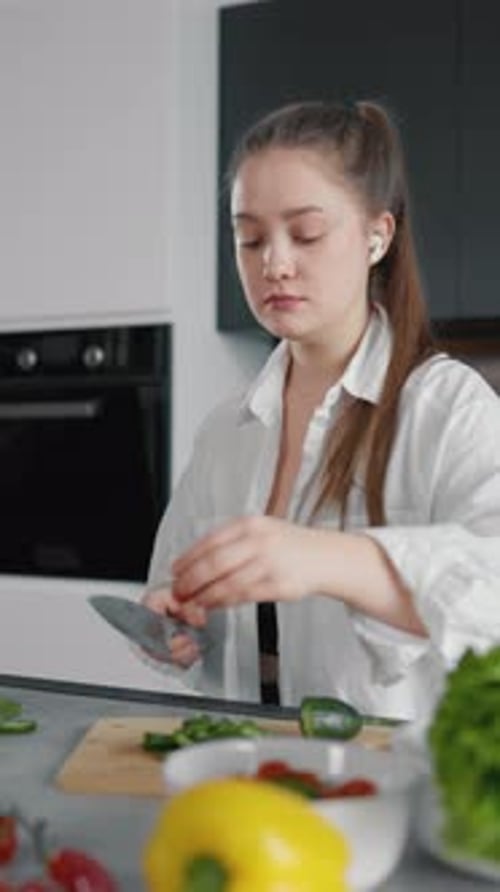 Woman in Kitchen Chopping Vegetables and Listening Music