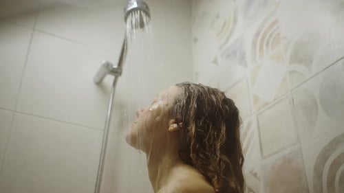 Junge Frau genießt eine entspannende Dusche im gefliesten Badezimmer