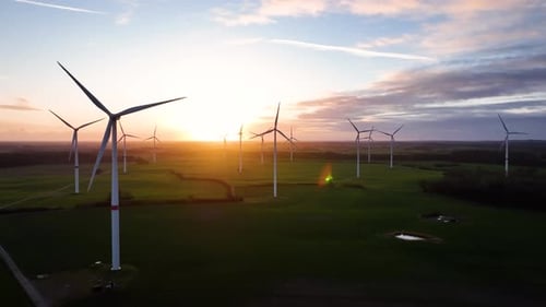 Aerial footage of sunrise with large spinning wind turbine in agriculture fields.