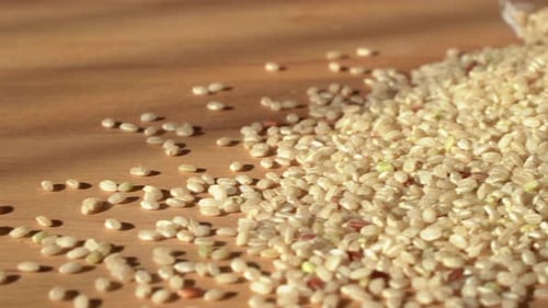 Slow dolly movement from left to right. Brown rice on a wooden table. Close up. Raw rice out of the