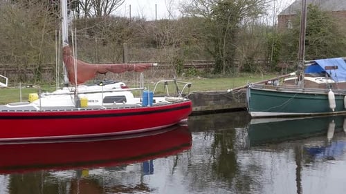 Small red green sailboats moored on narrow rural countryside canal marina