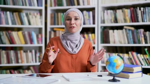 Webcam view. Muslim female teacher in hijab giving video call lesson in campus library space.