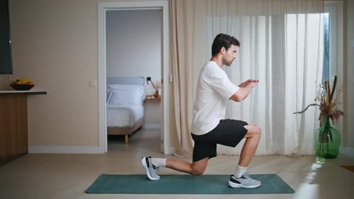 Young Man Doing Lunges on a Yoga Mat Indoors