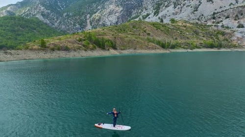 Aerial View Paddleboarders Glide Through Emerald Waters Surrounded By Rugged Peaks and Surreal Dry