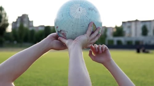 Arms Holding a Globe on a Grassy Field
