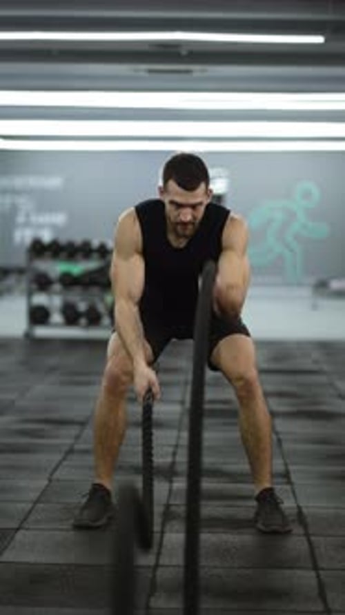 Attractive Muscular Man Working Out in the Gym Using Battle Ropes with High Intensity