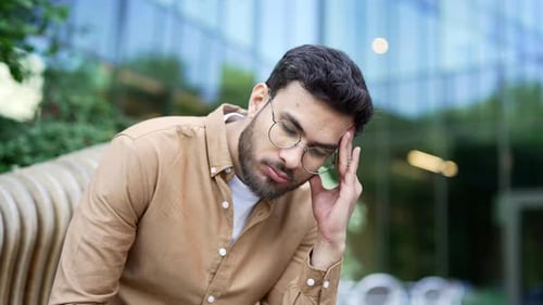 Businessman has depression suffering from mental pain sitting on a bench near a business office