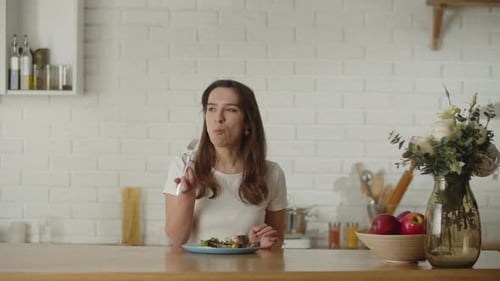A Longhaired Brunette Woman Sits Down at the Table to Have Breakfast with a Vegetable Salad A