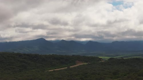 Drone view over green forest, mountains in distance, cloudcover