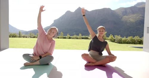 Practicing yoga, two women sitting on mats outdoors in serene mountain setting
