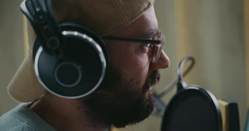 Close Up Focused Bearded Podcast Host Wearing Cap and Studio Headphones Speaks Confidently