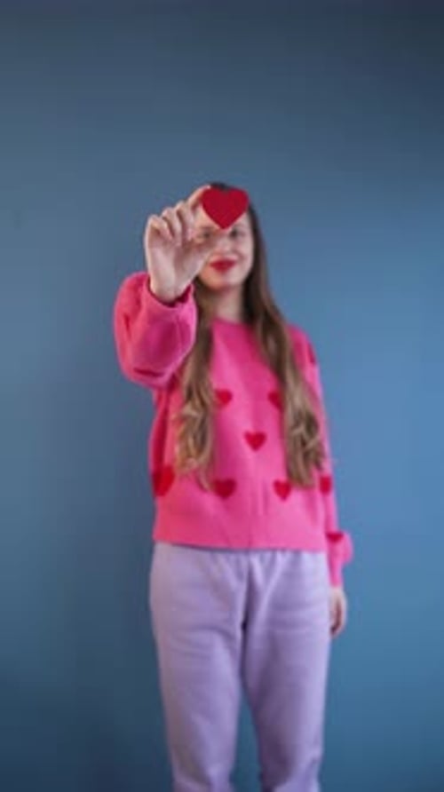 Happy Young Woman Holding Pink Heart Over Eye in Studio Valentine Concept Vertical