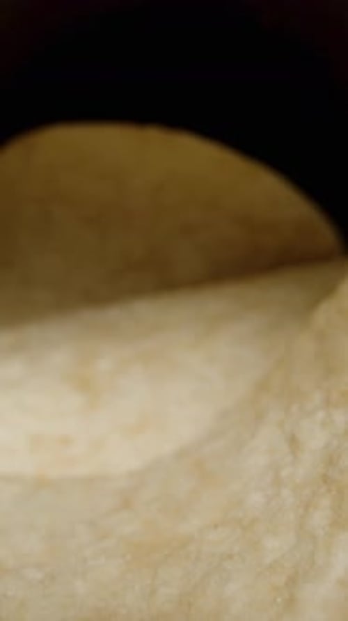 Vertical video. I take even saddle-shaped corn chips from a can, against a black background.