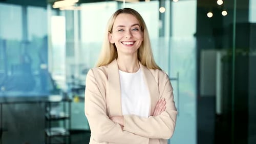 Portrait of a young smiling businesswoman standing in a modern office with crossed arms.