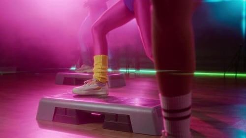 Women Exercising on Steppers in Studio with Pink Lights