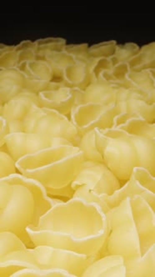 Dry pasta gnocchetti rotates, evenly scattered on a plate, on a black background, close-up. View fro