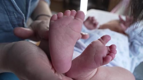 Loving Mother Holding Newborn Baby Feet in Hands