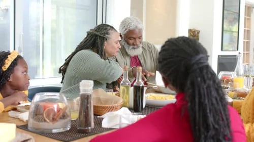 Diverse family initiating meal, passing pasta from communal bowl with wooden tongs at dining table