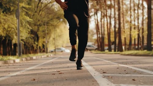 A Lowangle View Captures an Athlete Running in a City Park Alley on a Sunny Morning Epitomizing the